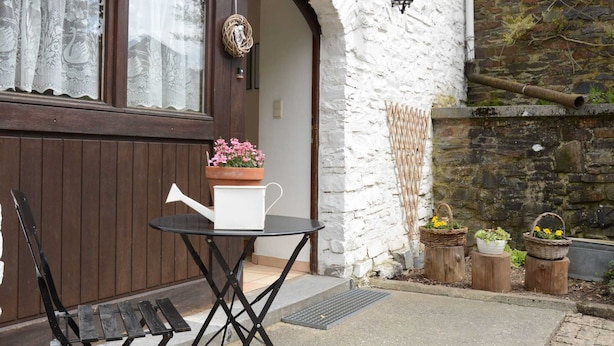 A wooden door with a white wall, a small table with a watering can, and potted plants.