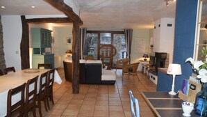 A spacious dining area with a long table and chairs, a cozy seating area with cushions, and a kitchen visible through an open doorway.