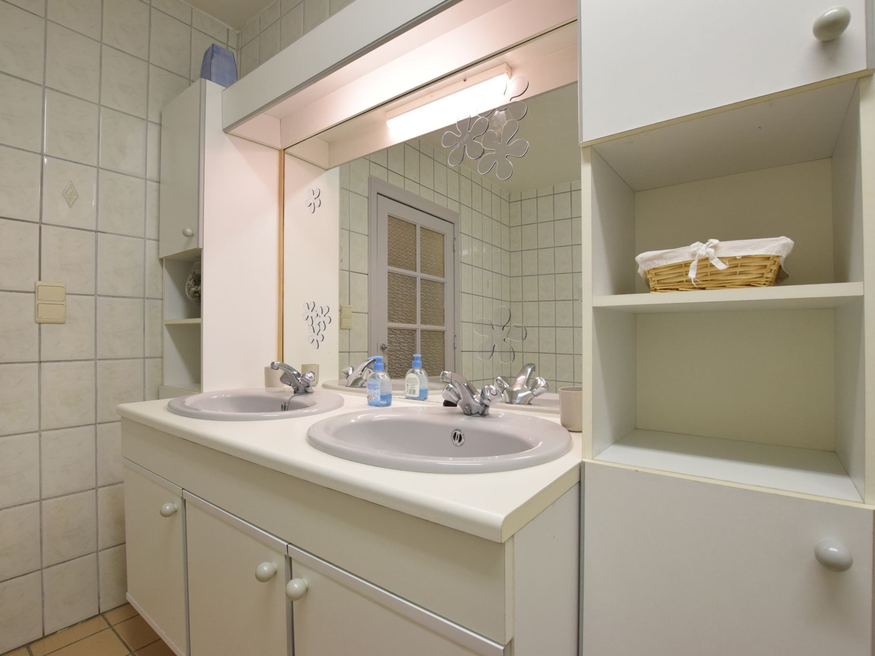 A bathroom with two sinks, a mirror, and a shelf with a basket.