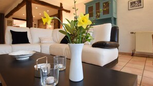 A living room with a white sofa, a black leather chair, a white vase with yellow flowers, and a black table with a white plate and glasses.
