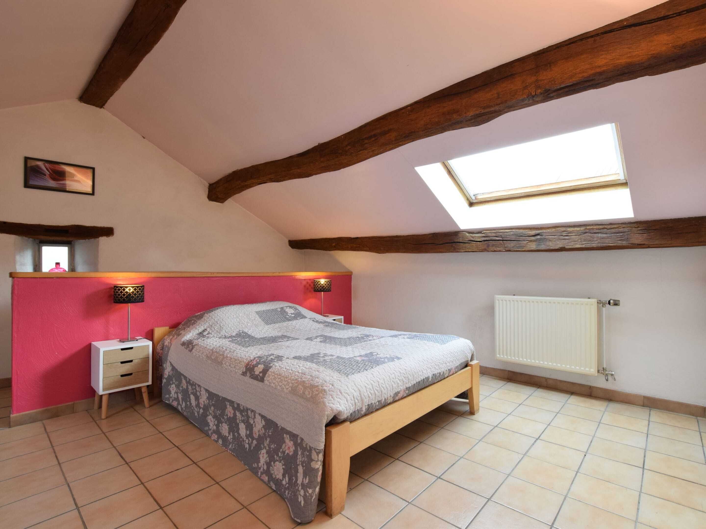 Une chambre avec un plafond en pente, un puits de lumière, un lit recouvert d’une couvre-lit à motifs, des lampes de chevet, une petite table de chevet et un radiateur.