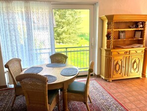A dining area with a round table, wicker chairs, a patterned rug, a wooden cabinet, and a view through a glass door. - Ferienwohnung in Bruchhausen mit Balkon (Lennestadt)