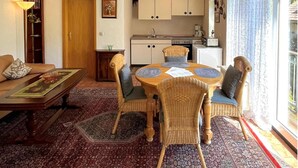 Uma sala de estar aconchegante com uma mesa de jantar, cadeiras, sofá, estante de livros e cozinha.