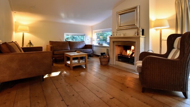 Un salon chaleureux avec une cheminée, un plancher en bois, un canapé, un fauteuil et une table.
