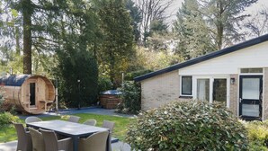 Un chalet rustique doté d’un grand sauna en bois, d’une terrasse avec des meubles en osier et, au fond, d’une maison en briques.