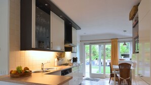 Une cuisine moderne dotée d’un grand îlot central, d’un coin repas avec une table et des chaises, et d’une porte-fenêtre coulissante donnant sur un jardin.