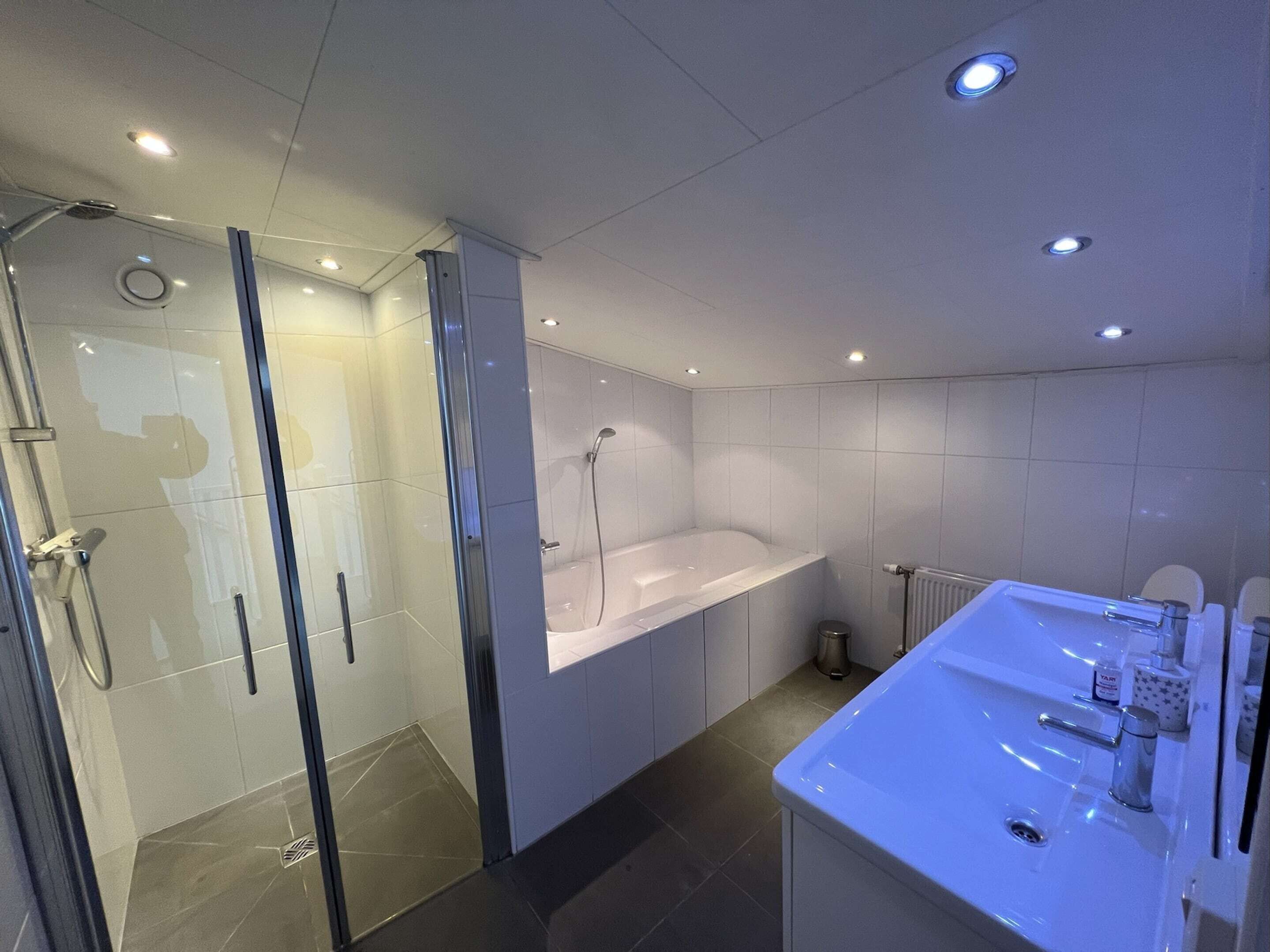 Un bagno moderno con doccia vetrata, una vasca freestanding e un lavandino spazioso con articoli da toilette.