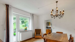 Ein großzügiger Essbereich mit Holztisch und -stühlen, einer Kristallleuchtre und Blick auf Grünpflanzen durch ein großes Fenster.