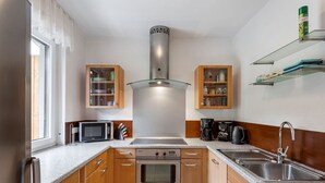 Eine kompakte Küche mit Holzausstattung, einem Edelstahlherd, einer Mikrowelle, einer Kaffeemaschine und einem Spülbecken.
