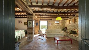 Un interior rústico con vigas de madera a la vista, una pared de piedra, un sofá, un sillón mecededor y una mesa de comedor.