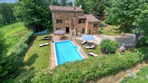 Una casa de piedra con piscina, rodeada de abundante vegetación y árboles.