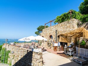 Ein Steinhaus mit Außenbestuhlung, Sonnenschirmen und Blick auf die Landschaft.
