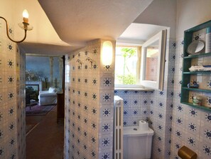 Ein Badezimmer mit gemusterten Fliesen, einer Toilette, einem Fenster und einem Ablagefach mit Toilettenartikeln.