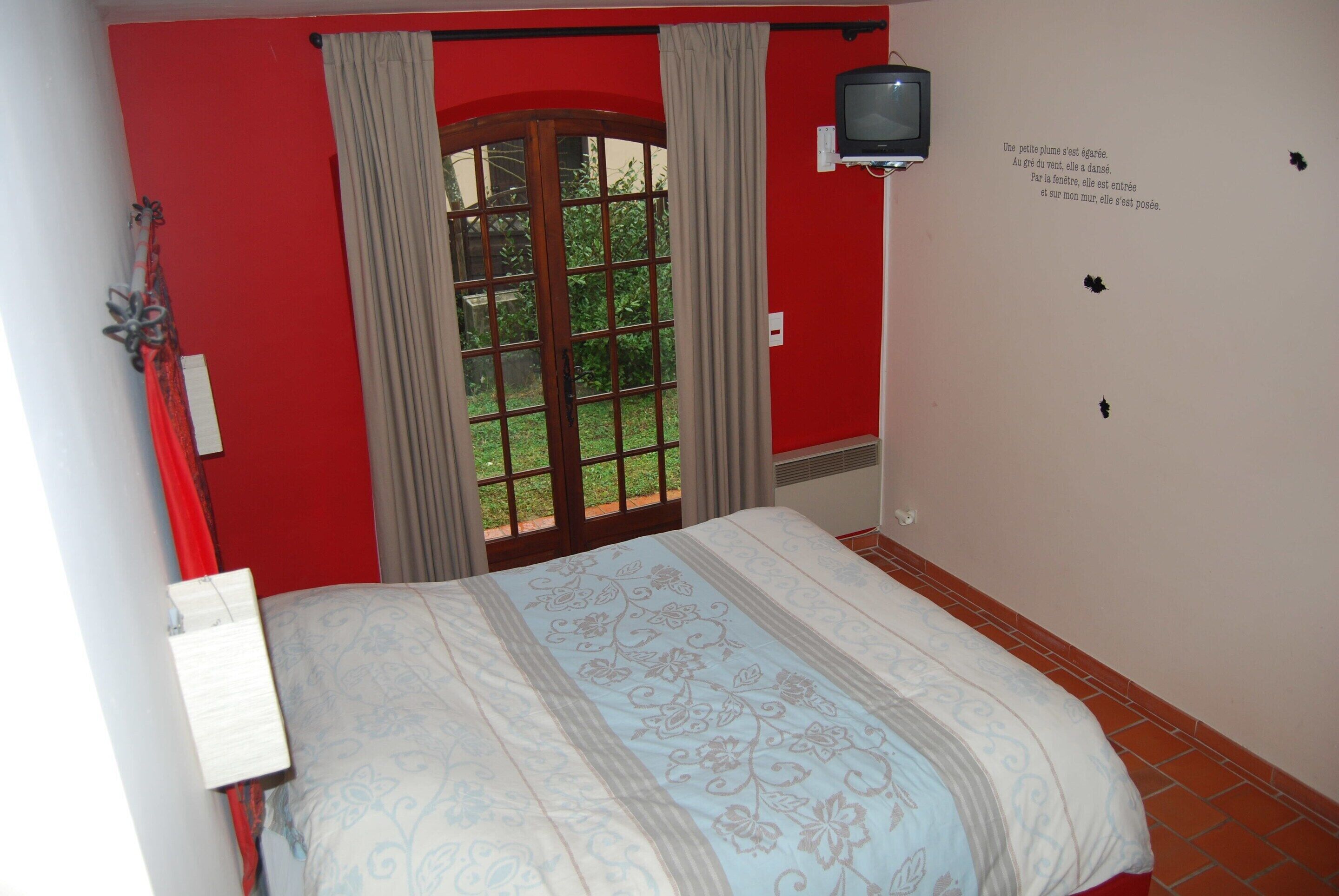 A bedroom with a bed, a window with curtains, a television mounted on the wall, and a small decorative item on the wall.