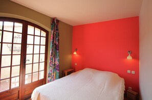 Een slaapkamer met een groot raam, een bed, een klein tafeltje en een rode muur.