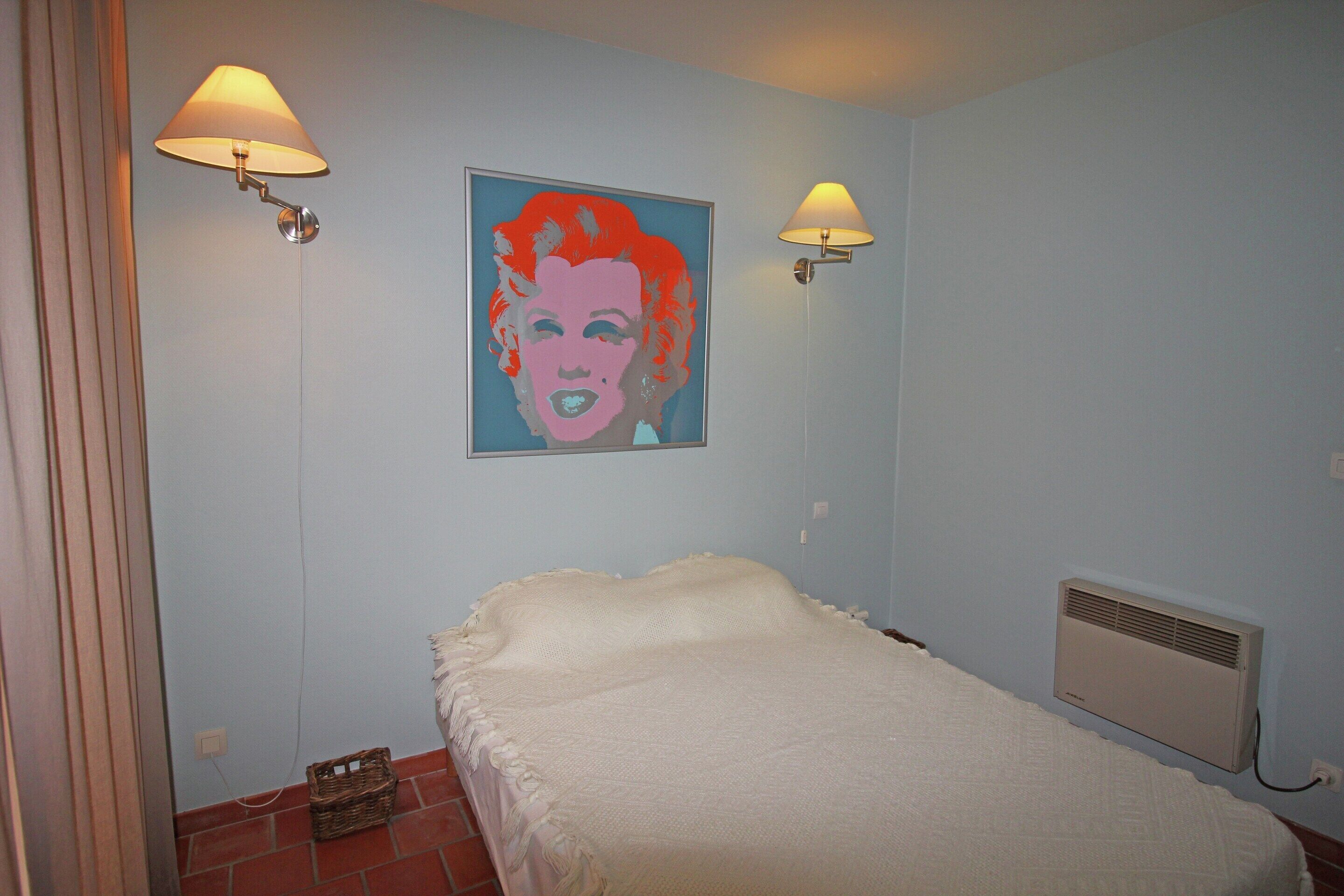 Quarto com cama, duas luminárias na parede, um radiador e uma obra de arte emoldurada.