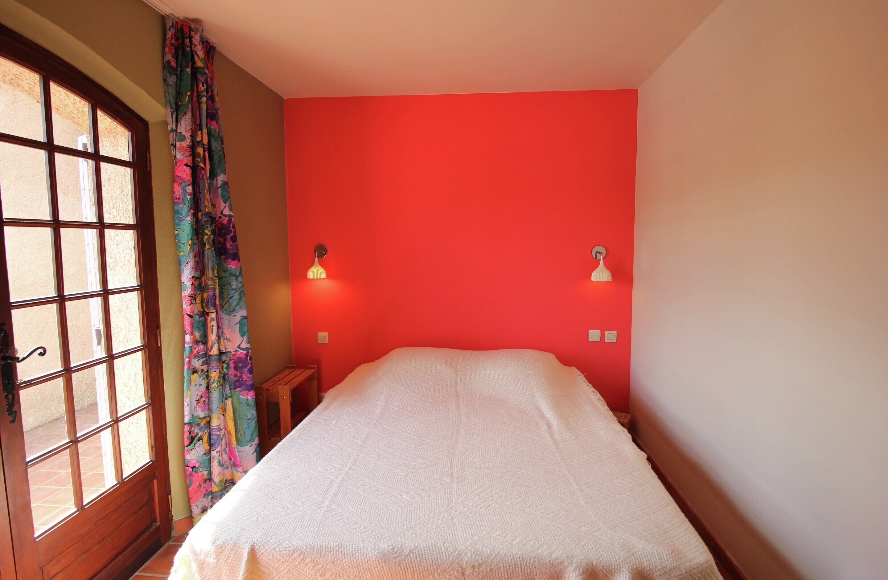 A room with a bed, a window with curtains, and two wall-mounted lights.