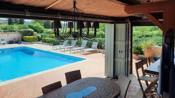 Ein Außenpoolbereich mit Liegestühlen, einem Tisch und einem Deckenventilator.