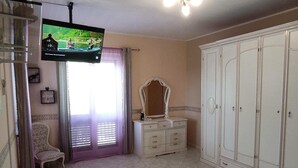 Ein Schlafzimmer mit Fernseher, Schminktisch mit Spiegel, Kleiderschrank und Stuhl.