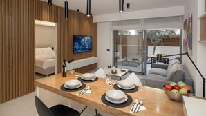 Un espace repas moderne avec une table en bois dressée pour quatre personnes, un téléviseur fixé au mur et une vue sur la terrasse extérieure.