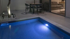 Un espace piscine extérieur moderne, comprenant une table et des chaises, un arbre et une porte vitrée donnant sur un salon.