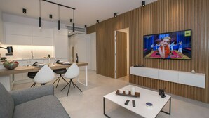 Un salon moderne doté d’un téléviseur à écran plat, d’un coin repas avec une cuisine en arrière-plan et d’un canapé.