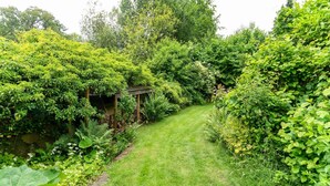 Un jardin luxuriant avec un sentier dallé menant à une pergola en bois.