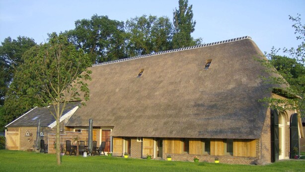 A large building with a thatched roof, a brick lower section, and a small window. - Farmhouse in Geesteren Near Forests (Geesteren)