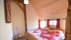 A bedroom with a wooden bed, a chair, a window with curtains, and a wooden ceiling. - Farmhouse in Geesteren Near Forests (Geesteren)