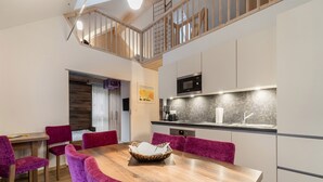 Un comedor moderno con una mesa de madera y sillas moradas, una cocina con microondas y fregadero, y una escalera que sube a un nivel superior.