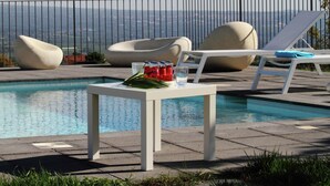 Un espace aménagé au bord de la piscine, avec des chaises longues, une table où sont servis des boissons et une vue sur la ville.