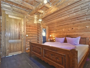 A log cabin bedroom with a wooden bed, a nightstand, and a window. - Wooden Holiday Home With Sauna (Teunz)