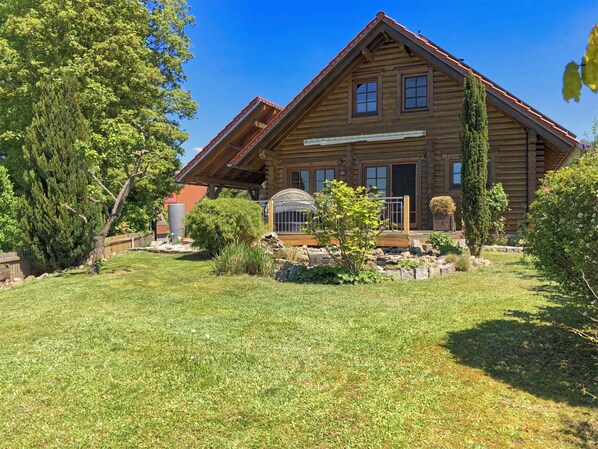 A log cabin with a sloped roof, a large front window, and a covered porch area.