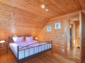 A wooden-paneled room with a bed, a nightstand, and a wall-mounted lamp.