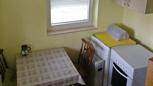 A compact kitchen with a window, a table with a checkered tablecloth, a wooden chair, a white refrigerator, and a white oven. - Enjoy the nature on Zlatibor (Zlatibor)
