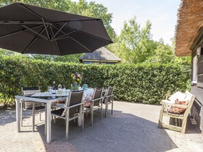 An outdoor patio with a table set for dining, chairs, a large umbrella, and a thatched-roof structure. - Farmhouse in Balkbrug With Sauna (Balkbrug)