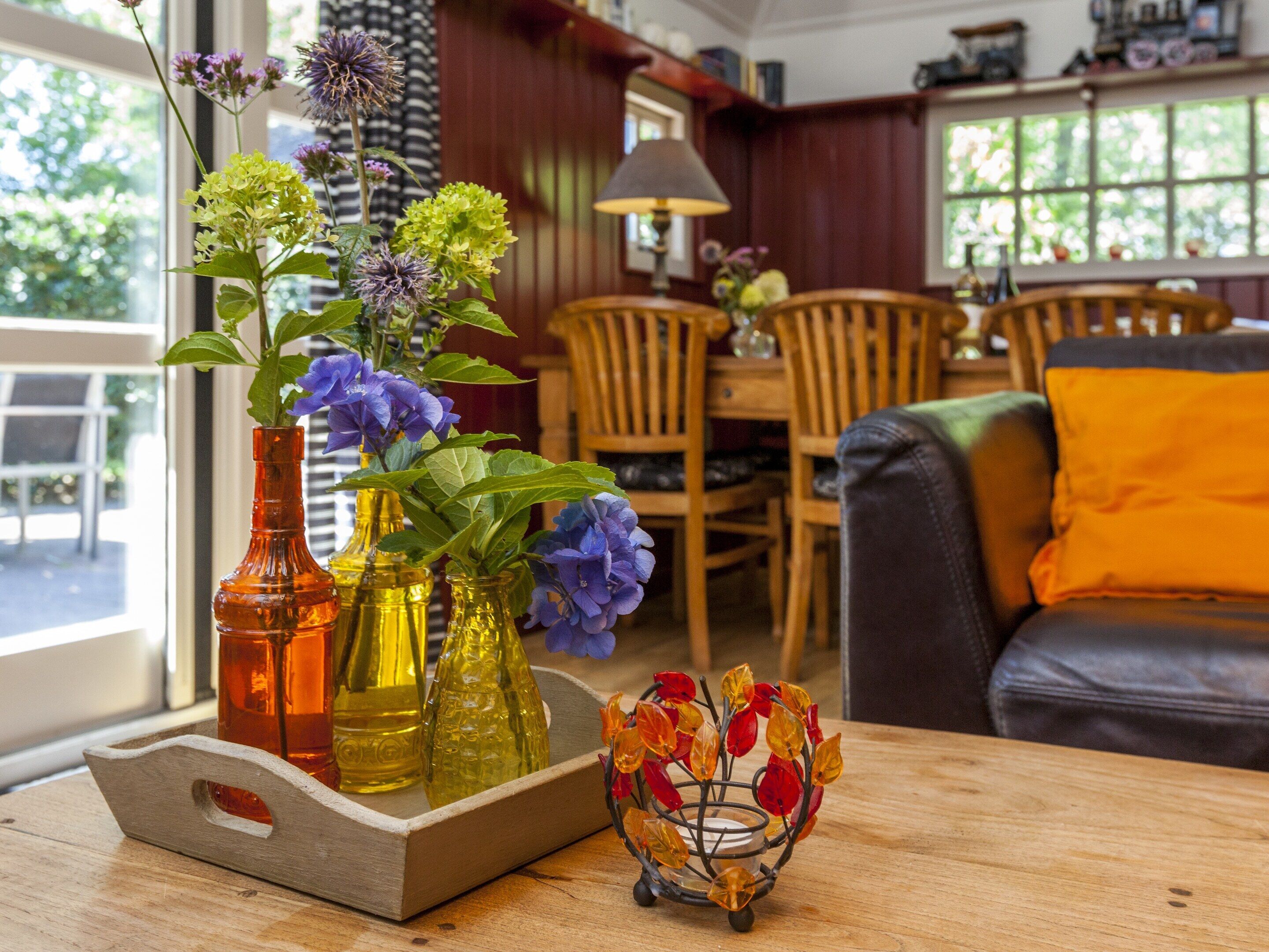 A wooden table with glass vases containing flowers, a decorative metal bowl, and a dining area with wooden chairs and a table.