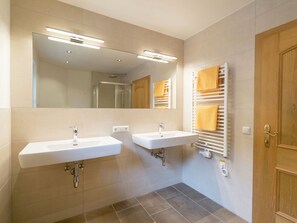 A modern bathroom with two sinks, a shower, and a towel rack with yellow towels. - Apartment With Terrace (Viehhofen)