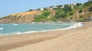 Une plage avec un rivage rocheux, des vagues et une colline où se trouvent des maisons.