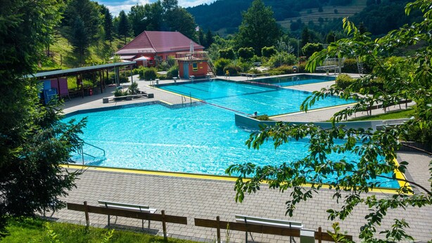 A swimming pool with a lifeguard tower and a pavilion, surrounded by lush greenery and hills. - Ferienwohnung mit Sauna in Schonbrunn Thuringen (Schleusegrund)