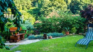 A garden with a wooden bench, a striped lounge chair, and a variety of potted plants. - Ferienwohnung mit Sauna in Schonbrunn Thuringen (Schleusegrund)