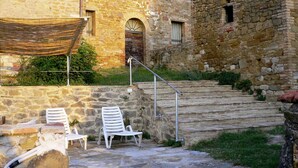 Ein Steinhaus mit einer Treppe, die zu einer Tür führt, zwei weiße Plastikstühle und einem Metallgeländer.