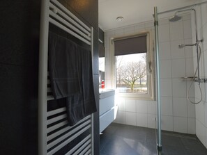 A modern bathroom with a glass shower, a towel rack, and a window with a view of trees.