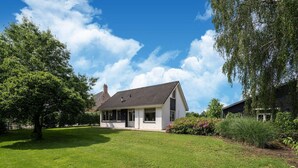 A single-story house with a sloped roof, surrounded by a well-maintained lawn and a large tree. - Cozy Holiday Home in Nistelrode With Garden (Nistelrode)