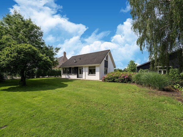 A single-story house with a sloped roof, surrounded by a well-maintained lawn and a large tree.
