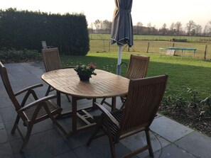 A round wooden table with four chairs, a potted plant, and an umbrella.
