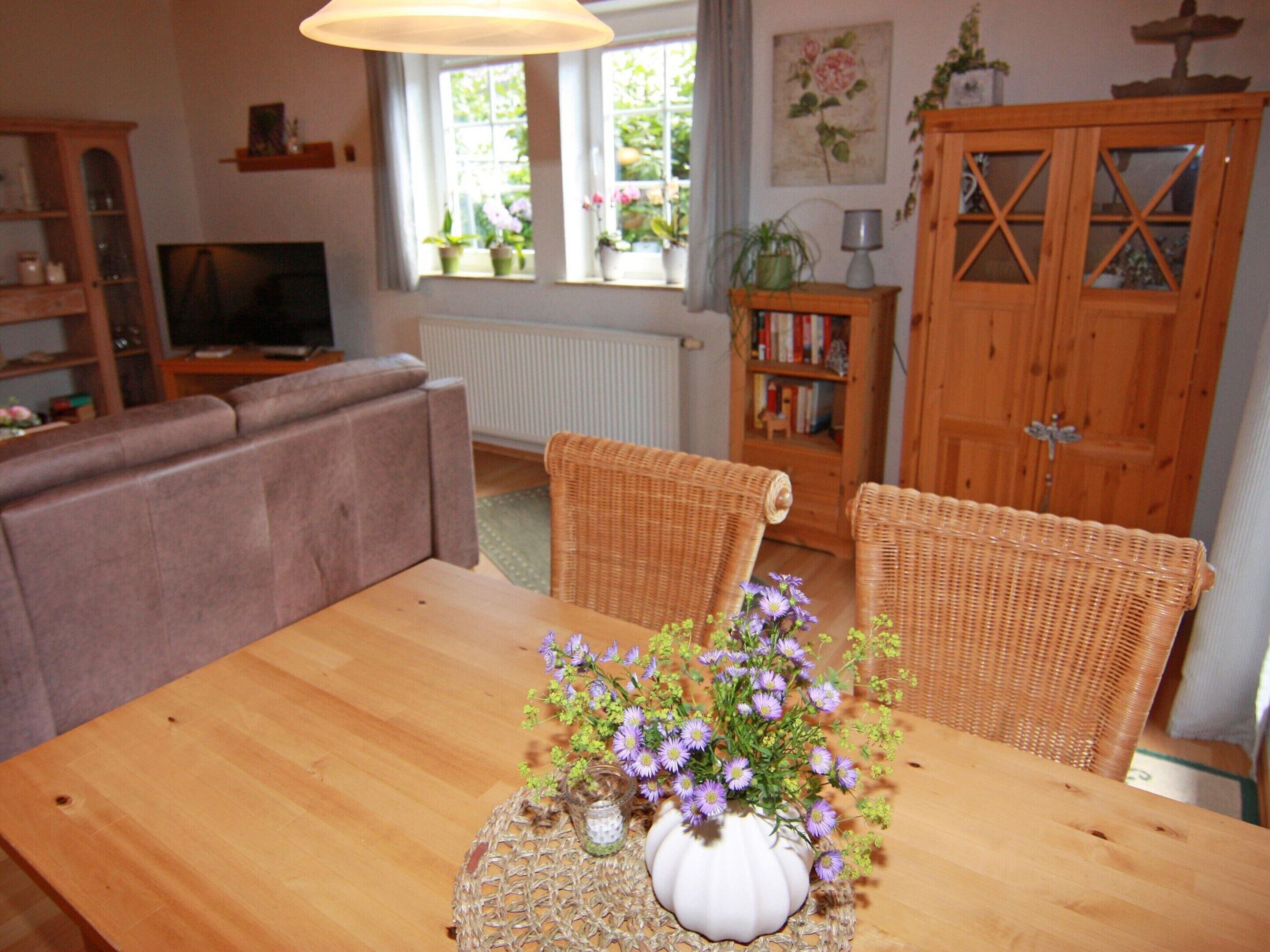 Un coin repas avec une table en bois, des chaises en osier et un vase de fleurs.