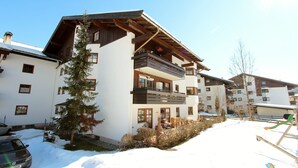 A multi-story building with balconies, a car parked in front, and snow on the ground. - Mountain View Apartment in Going am Wilden Kaiser near Ski Area (Going am Wilden Kaiser)