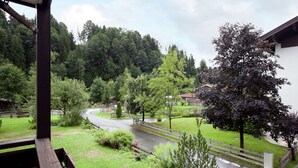 A view from a balcony overlooking a winding road through a green landscape with trees and a building in the distance. - Mountain View Apartment in Going am Wilden Kaiser near Ski Area (Going am Wilden Kaiser)