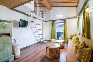 Un salon moderne avec un escalier en bois, un téléviseur fixé au mur et un canapé vert agrémenté de coussins à rayures.